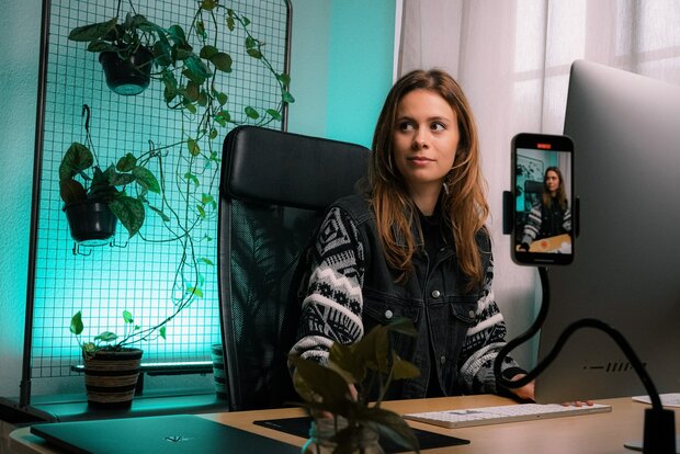  Social Media Akteurin filmt sich am Schreibtisch sitzend mit ihrem Smartphone.