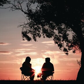 Zwei ältere Menschen sitzen bei Sonnenuntergang im Freien