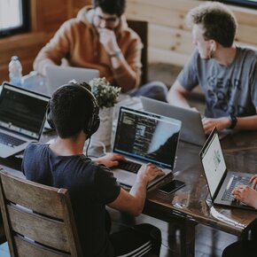 Schüler oder Studenten sitzen gemeinsamt an einem großen Tisch und arbeiten an Laptops