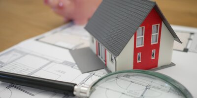Kleines Modell eines Hauses und eine Lupe liegen auf Steuerunterlagen