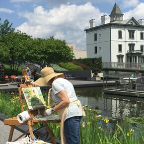 Künstlerin steht an einer Staffelei und malt im Freien