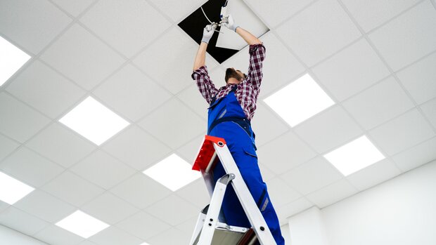  Handwerker steht auf einer Leiter und arbeitet an der Decke